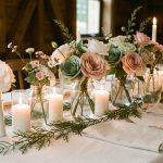 Table de mariage élégante et économique décorée de fleurs en papier, de bocaux en verre recyclés, de bougies blanches, de serviettes en lin et de feuillage.